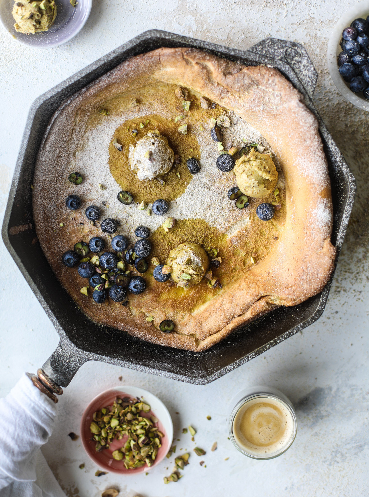This incredible dutch baby recipe is fluffy and light and perfect for breakfast! It's sprinkled with pistachio sugar and served with pistachio butter and fresh blueberries. It's super easy, simple and always a hit! I howsweeteats.com #dutch #baby #pistachio #blueberry #breakfast