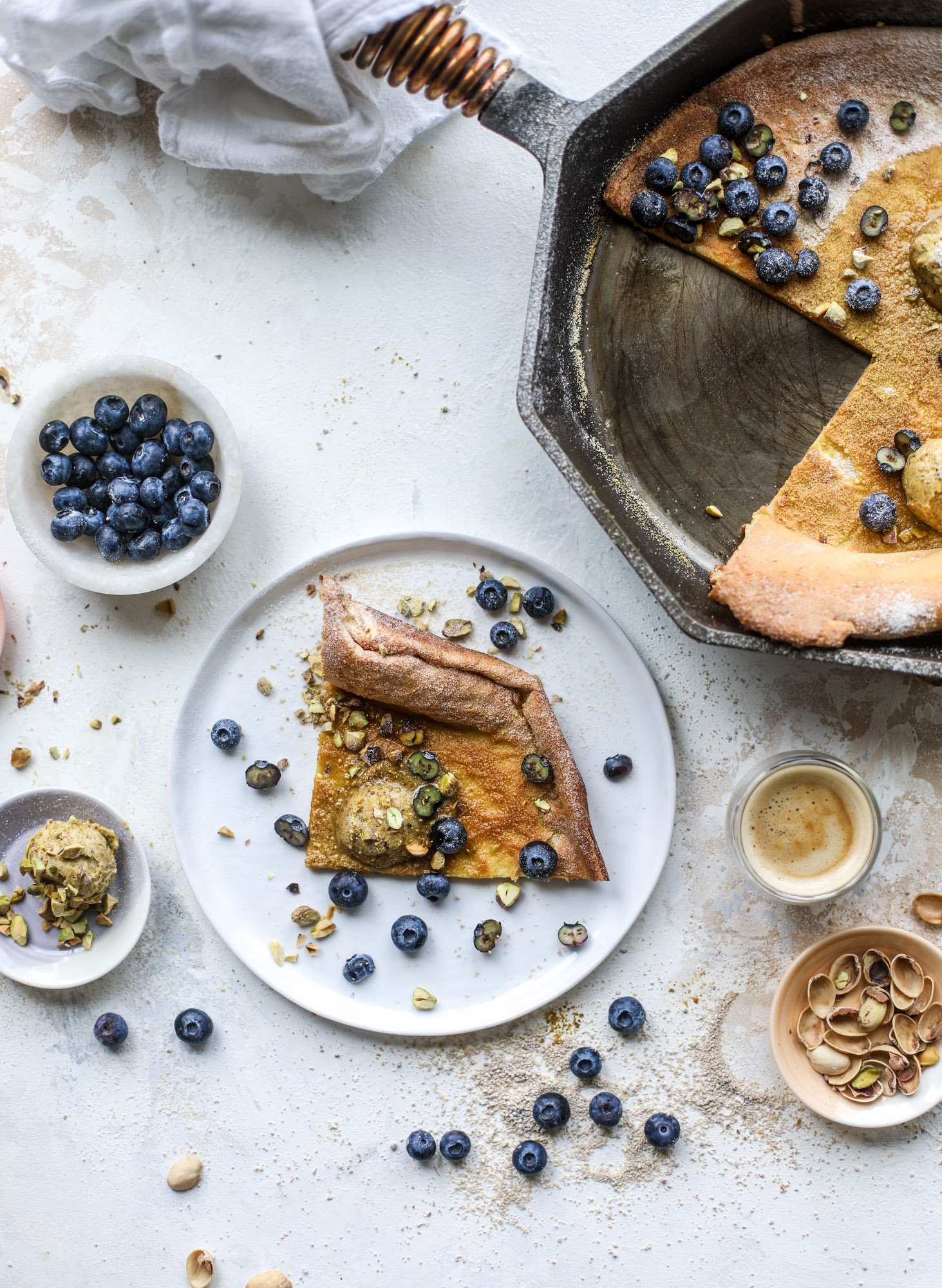 This incredible dutch baby recipe is fluffy and light and perfect for breakfast! It's sprinkled with pistachio sugar and served with pistachio butter and fresh blueberries. It's super easy, simple and always a hit! I howsweeteats.com #dutch #baby #pistachio #blueberry #breakfast