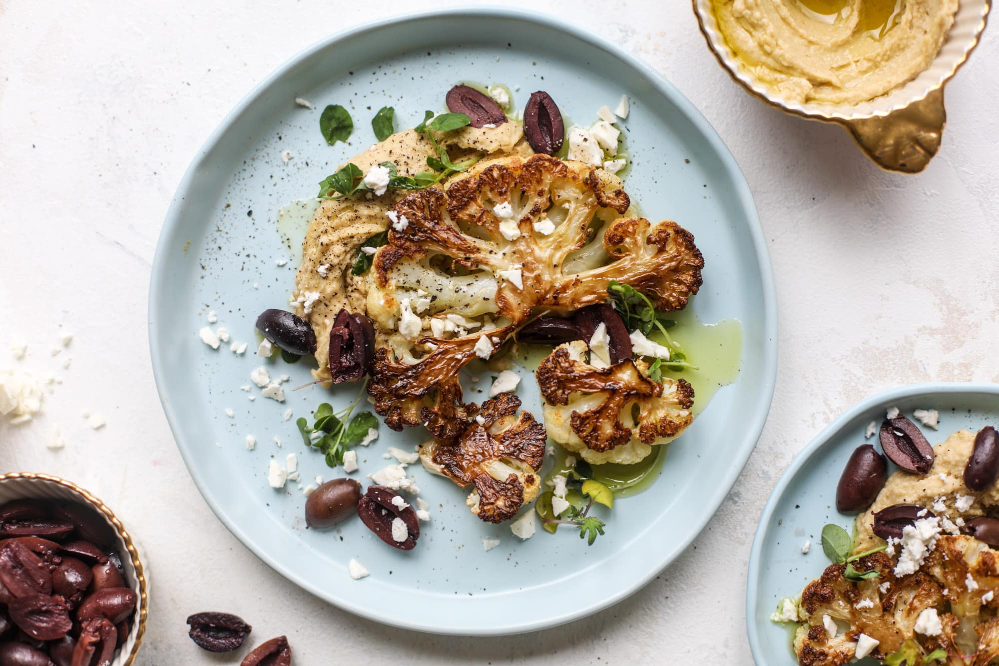 This roasted cauliflower with hummus, olives and feta is super flavorful and a wonderful meal, side dish or snack. Flavorful roasted cauliflower, creamy hummus, briney olives and tangy feta come together to make a major taste explosion. I howsweeteats.com #roasted #cauliflower #hummus #olives #feta