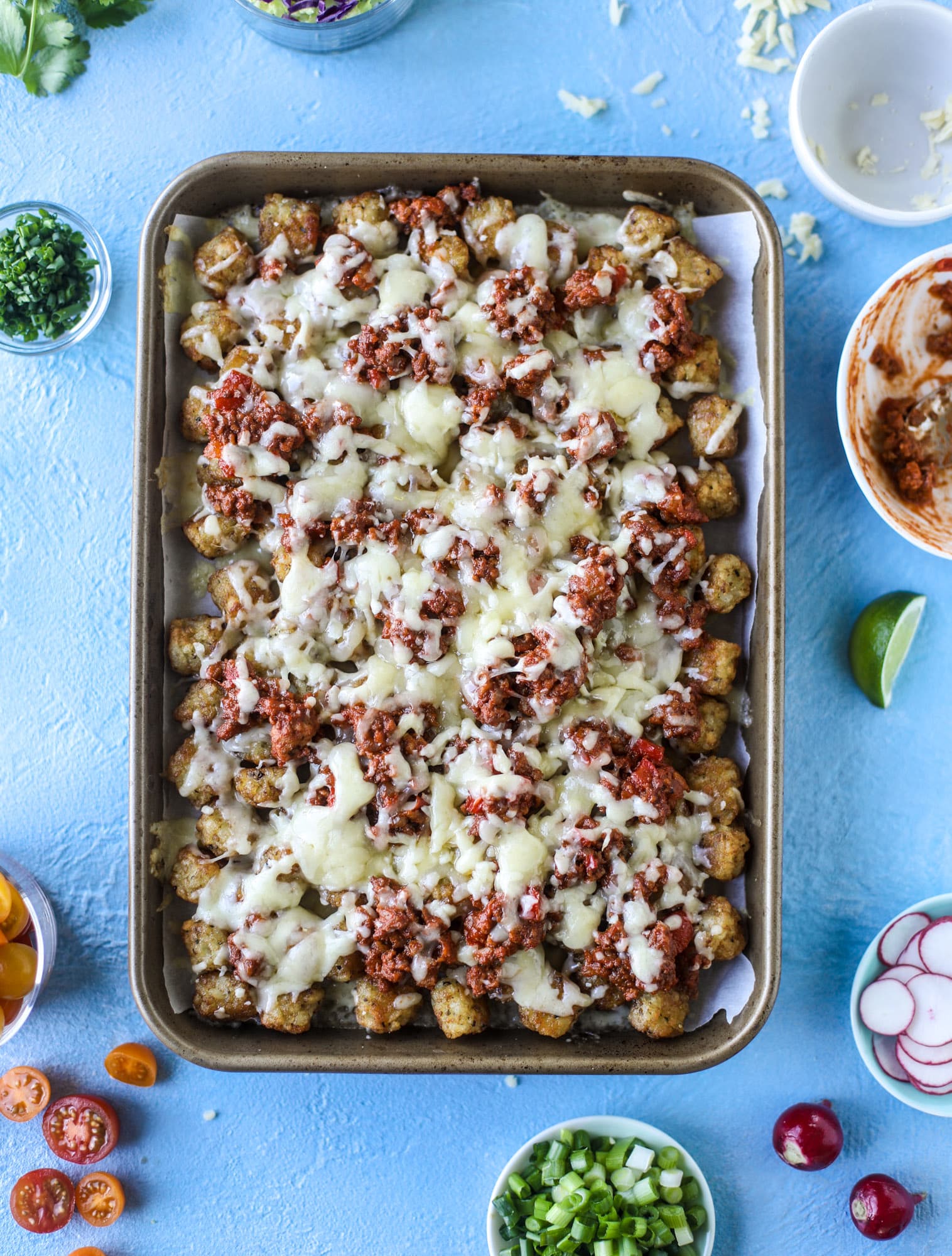 These tater tot nachos, otherwise known as totchos, are so delicious! They are cheesy and topped with a tangy, homemade sloppy joe mixture. Melted cheese, fresh tomatoes, scallions and chives come together for the best party food. I howsweeteats.com #totchos #tater #tot #nachos #sloppy #joes