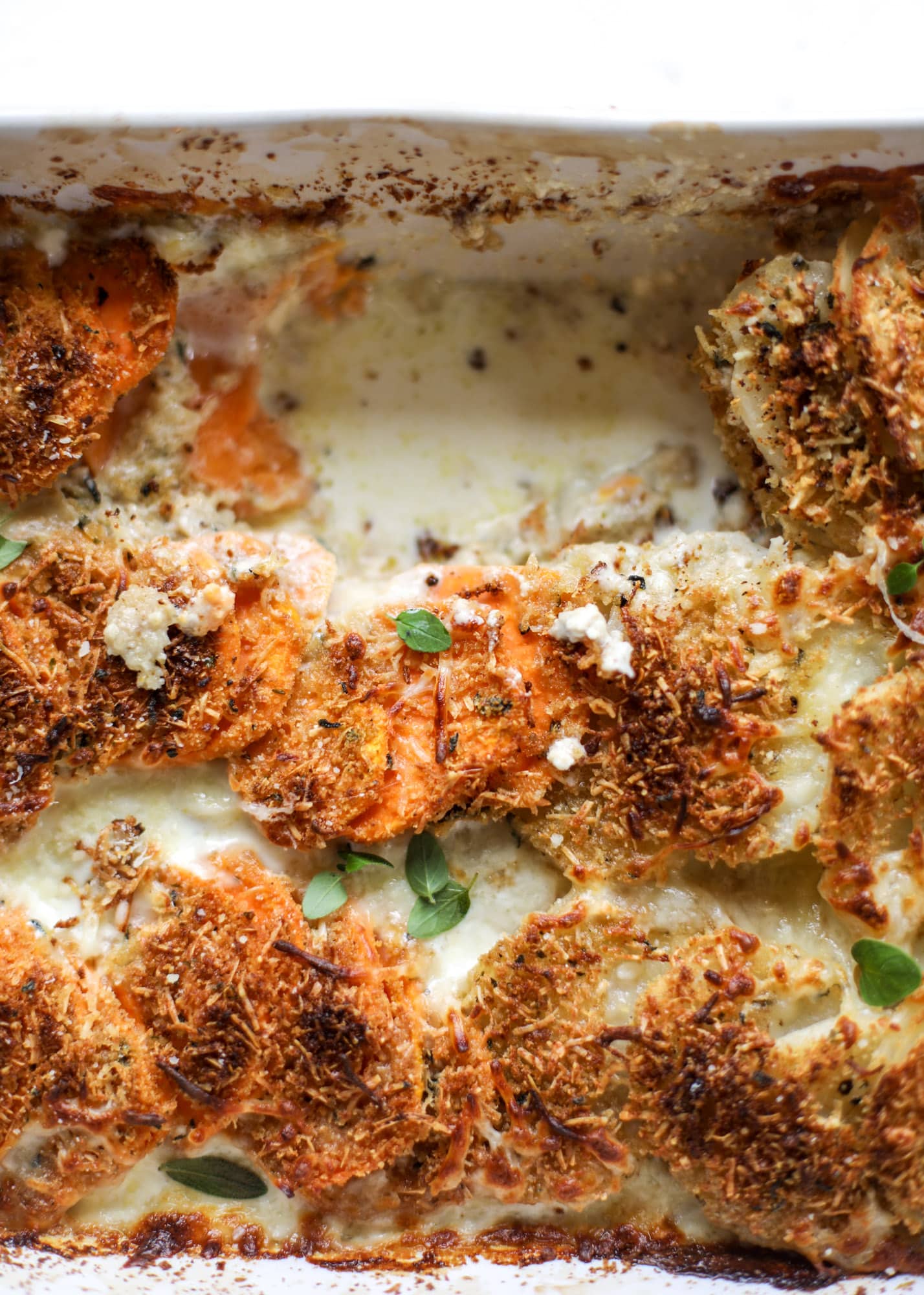 These scalloped potatoes are a cheese lover's dream. Sharp asiago and cream envelops idaho and sweet potatoes in these scalloped potatoes to please everyone! The crunchy asiago topping is irresistible. I howsweeteats.com #scalloped #potatoes