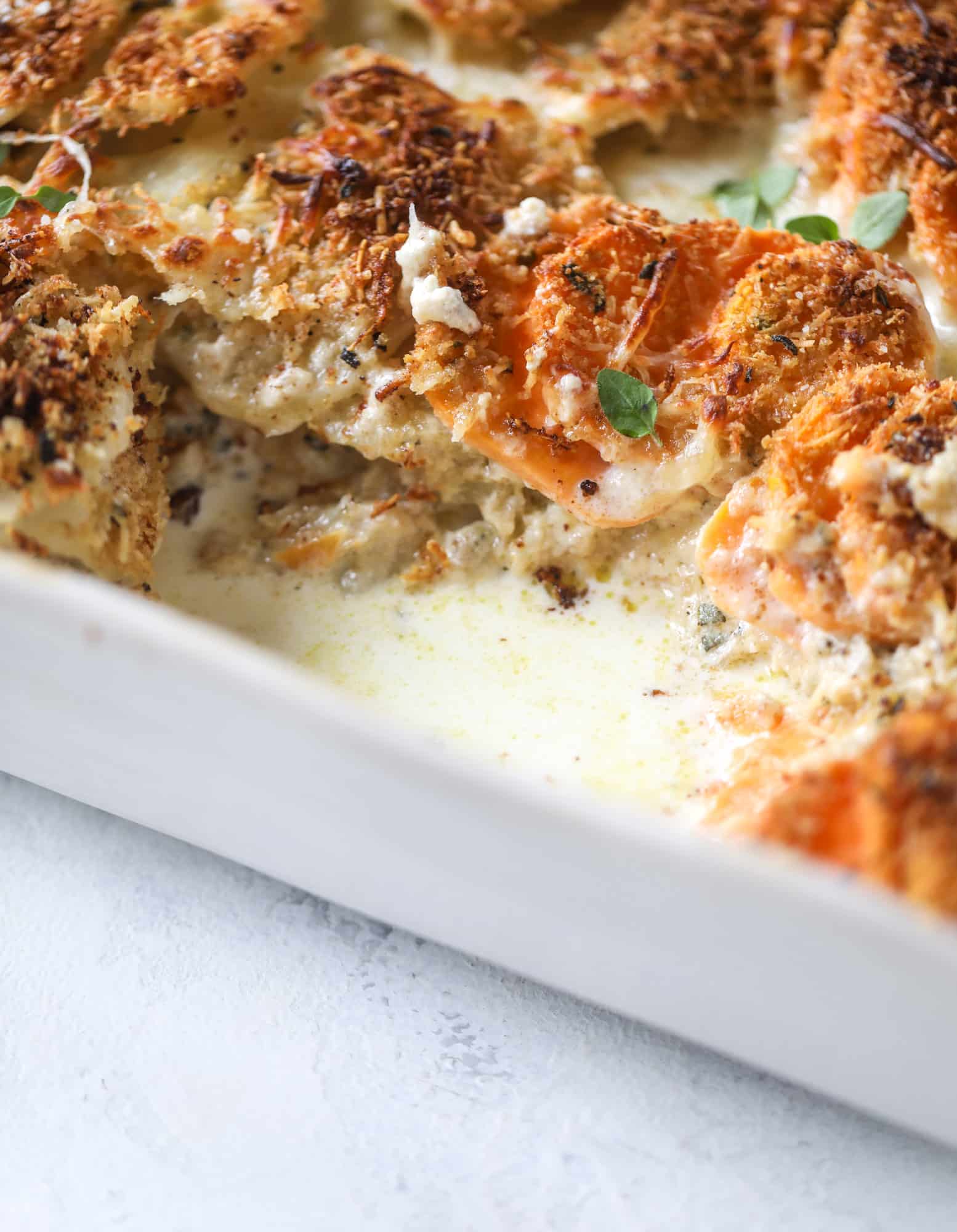 These scalloped potatoes are a cheese lover's dream. Sharp asiago and cream envelops idaho and sweet potatoes in these scalloped potatoes to please everyone! The crunchy asiago topping is irresistible. I howsweeteats.com #scalloped #potatoes