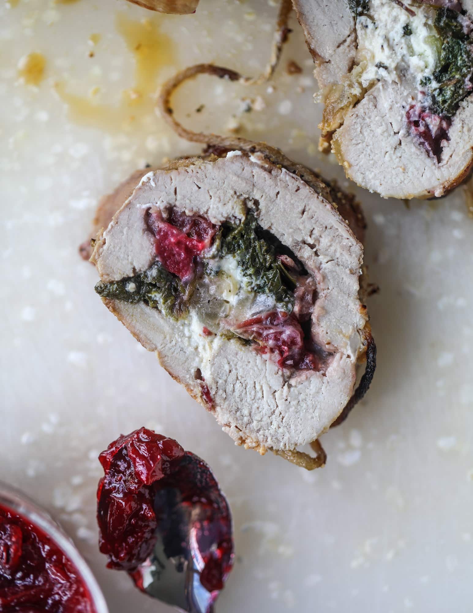 This holiday stuffed pork tenderloin is filled with caramelized onion, fresh cranberry sauce, goat cheese and fresh spinach. It's a show stopped and super delicious, along with being fairly simple to make! I howsweeteats.com #stuffed #porktenderloin