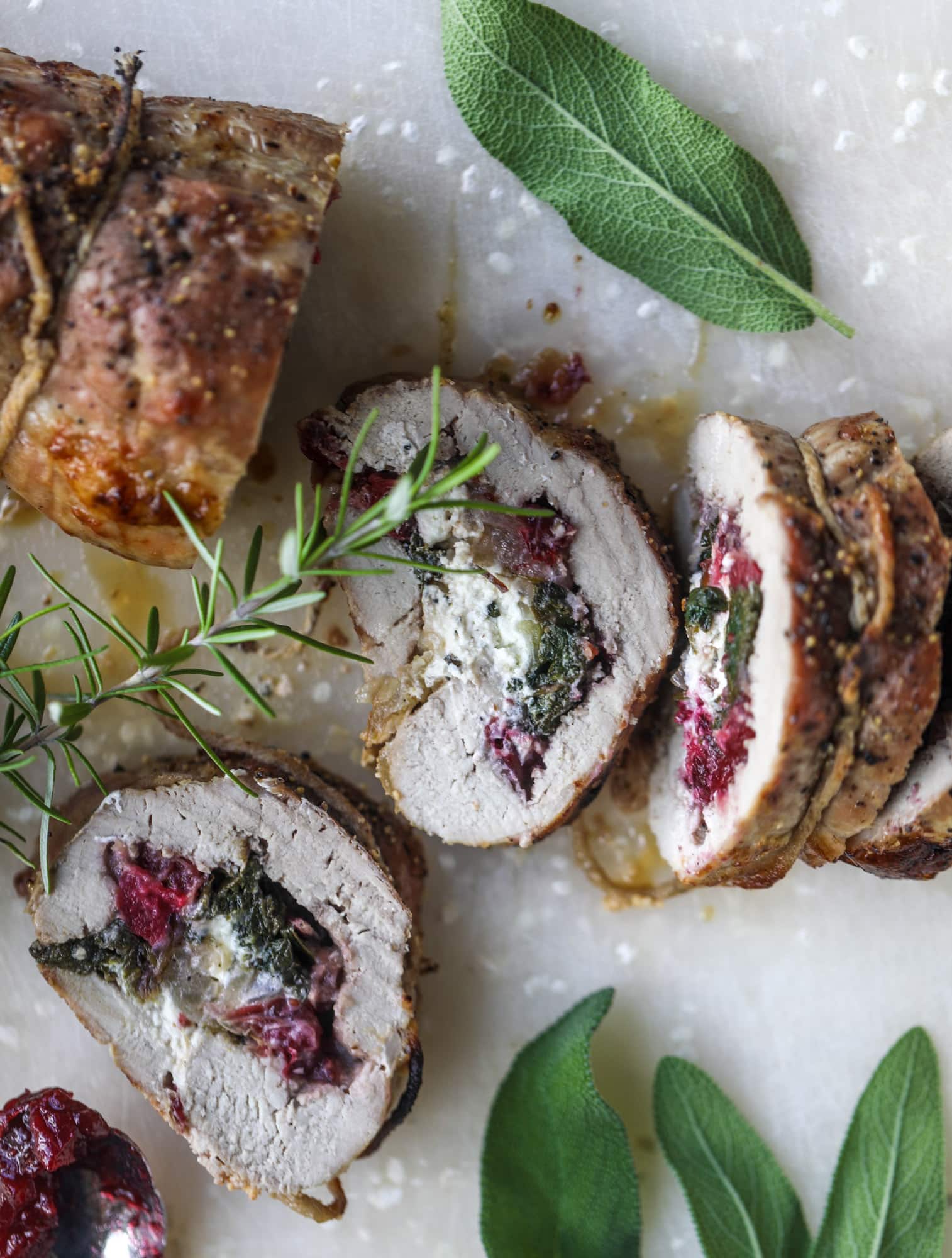 This holiday stuffed pork tenderloin is filled with caramelized onion, fresh cranberry sauce, goat cheese and fresh spinach. It's a show stopped and super delicious, along with being fairly simple to make! I howsweeteats.com #stuffed #porktenderloin