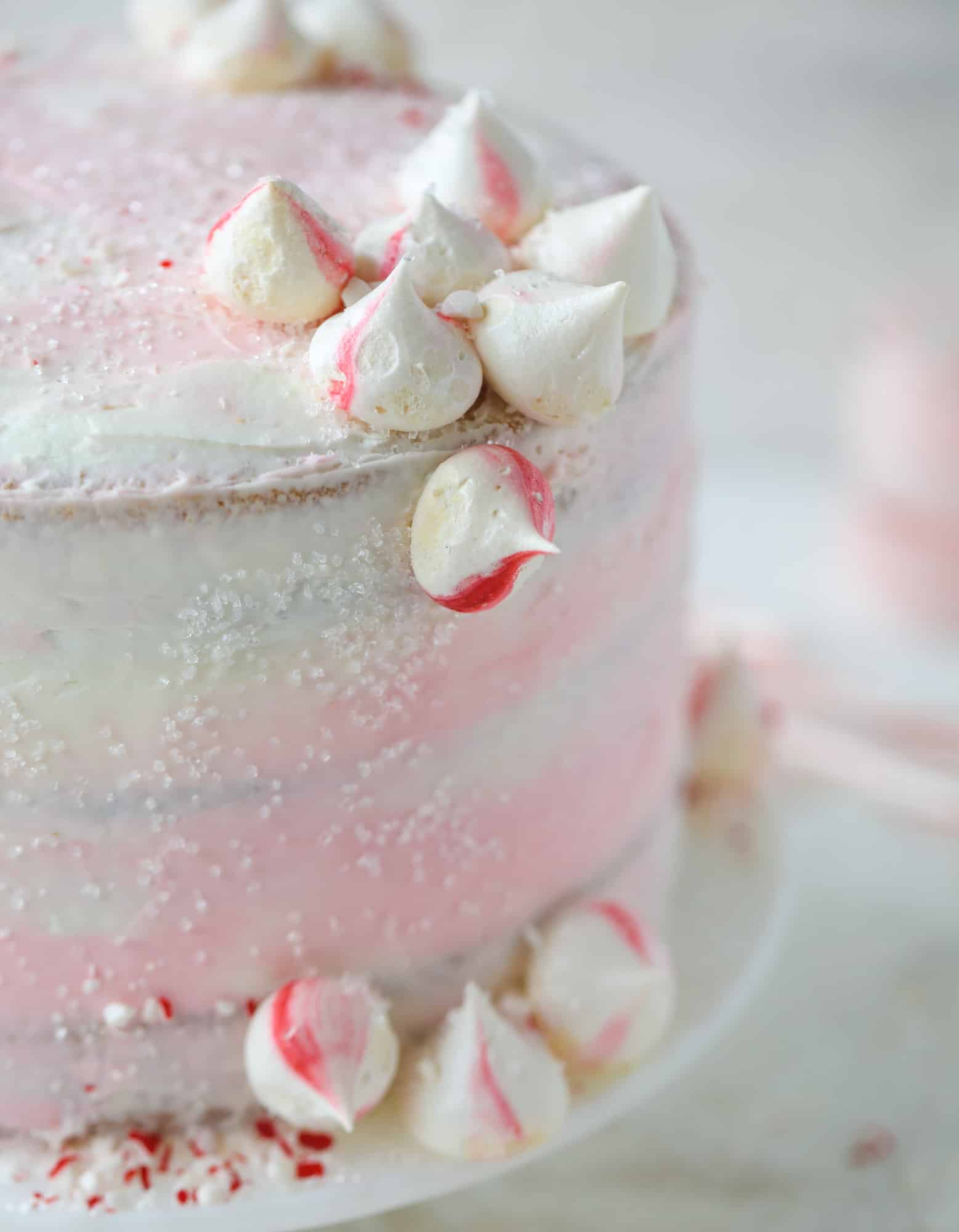 This pink peppermint cake is festive and delicious for the holidays! Layers of vanilla cake frosting with peppermint cream cheese frosting, covered in sparkly sugar and peppermint meringues. Couldn't be cuter! I #pinkpeppermint #cake
