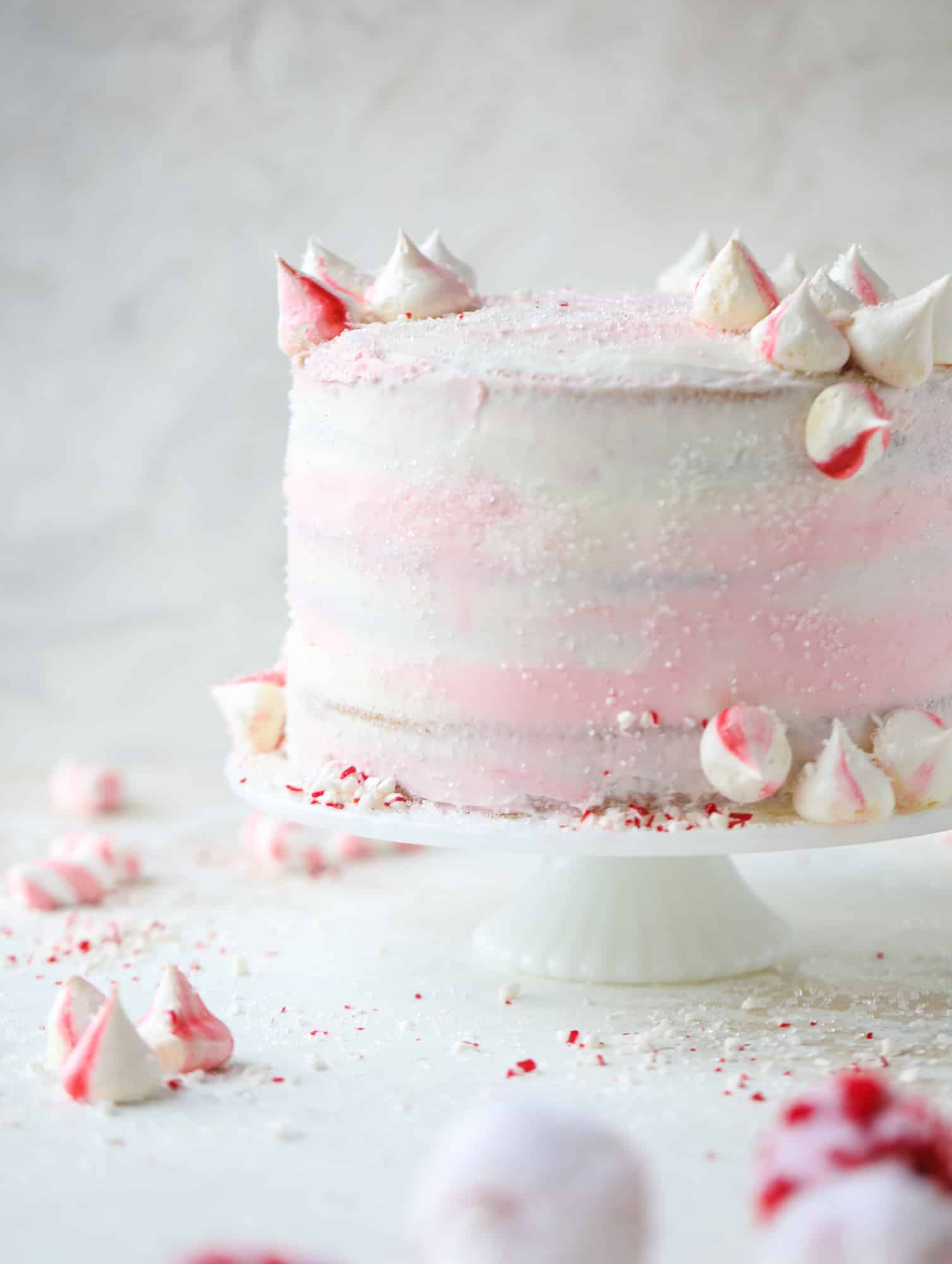 This pink peppermint cake is festive and delicious for the holidays! Layers of vanilla cake frosting with peppermint cream cheese frosting, covered in sparkly sugar and peppermint meringues. Couldn't be cuter! I #pinkpeppermint #cake