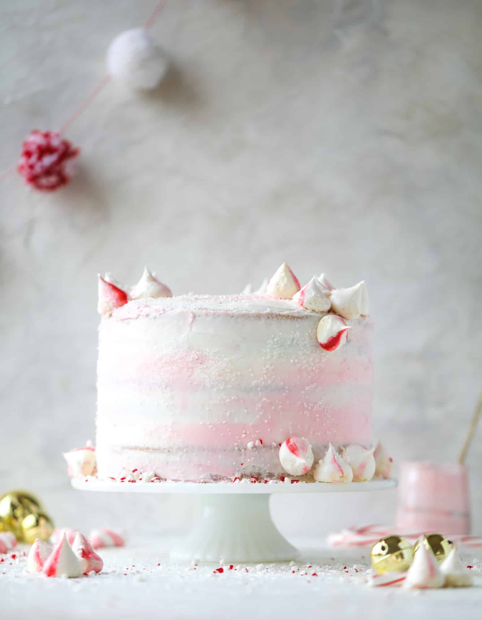 This pink peppermint cake is festive and delicious for the holidays! Layers of vanilla cake frosting with peppermint cream cheese frosting, covered in sparkly sugar and peppermint meringues. Couldn't be cuter! I #pinkpeppermint #cake