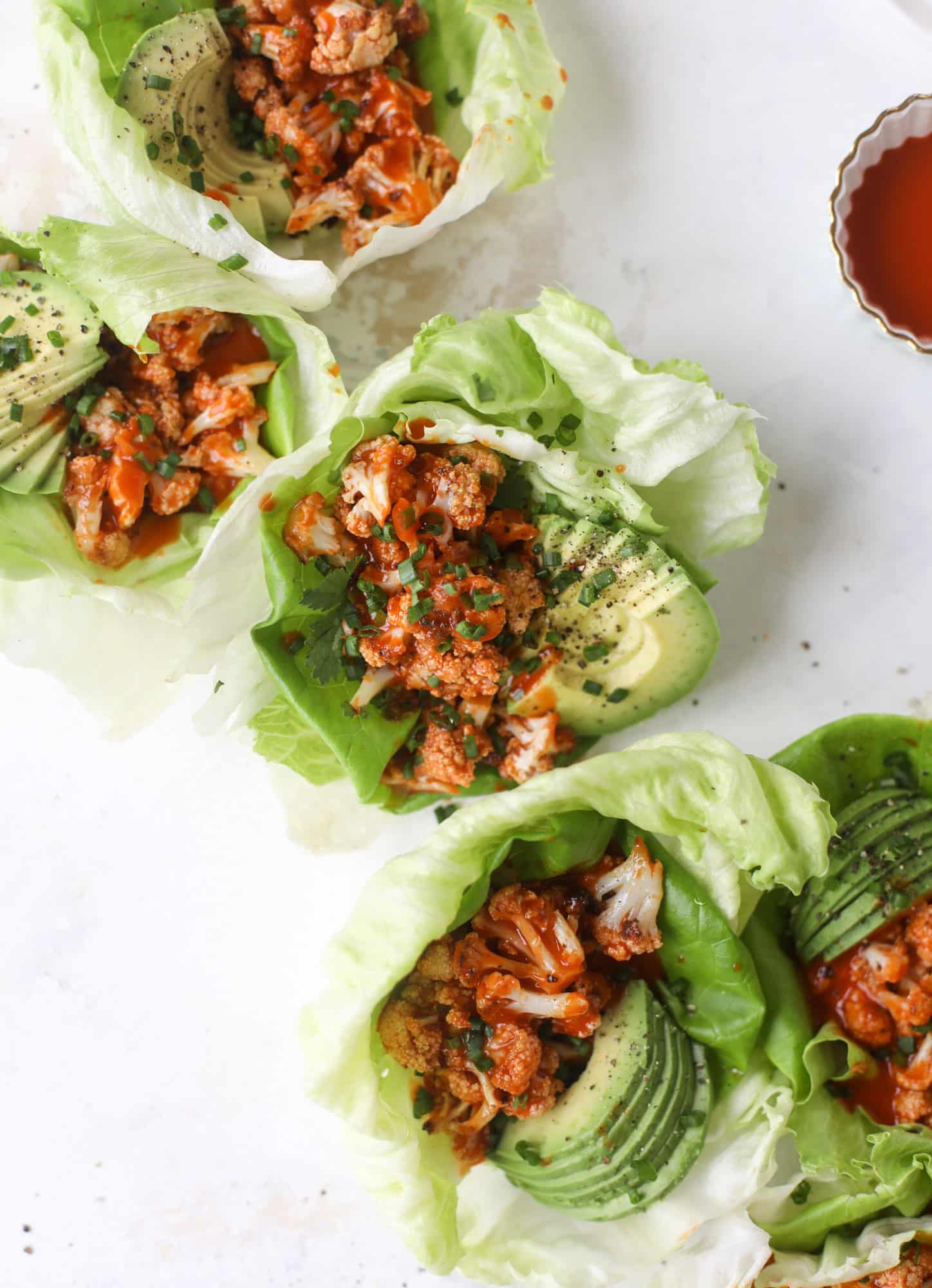 These buffalo cauliflower lettuce wraps are perfect for game day or even a quick weeknight dinner. Roasted cauliflower with buffalo wing sauce, sliced avocado, crumbled blue cheese, scallions, cilantro and chives makes for a flavor explosion! I howsweeteats.com #buffalo #cauliflower