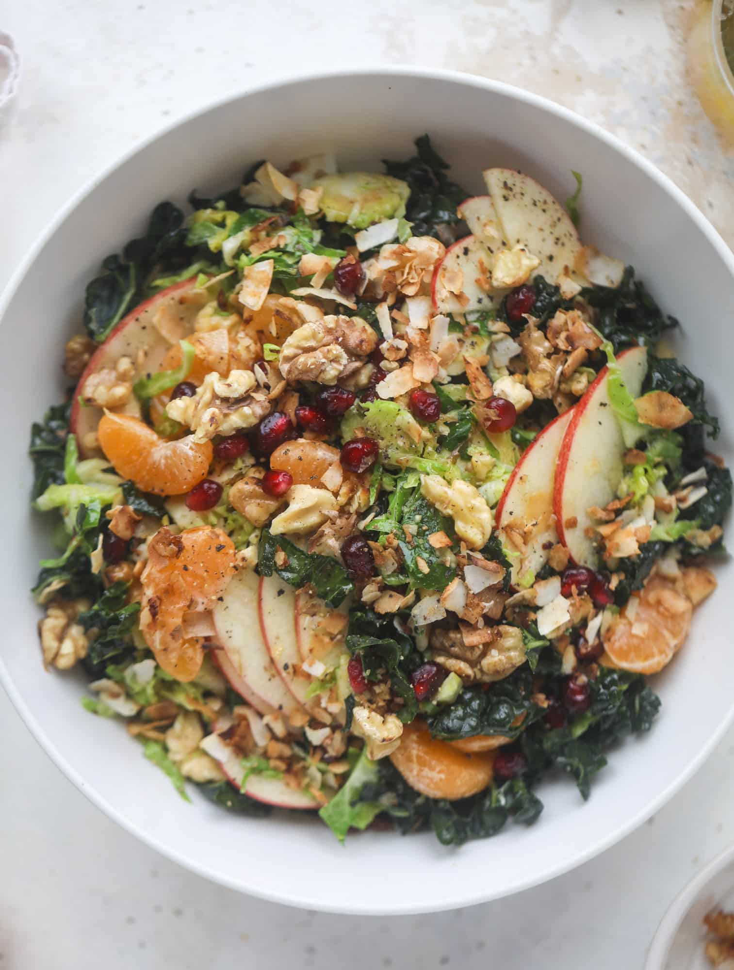 This winter crunch salad is loaded with tons of delicious, crunchy seasonal ingredients. A base of brussels sprouts and kale is topped with sliced apples, satsuma wedges, pomegranate arils, toasted walnuts and savory flaked coconut crunch. Delish! I howsweeteats.com #winter #salad