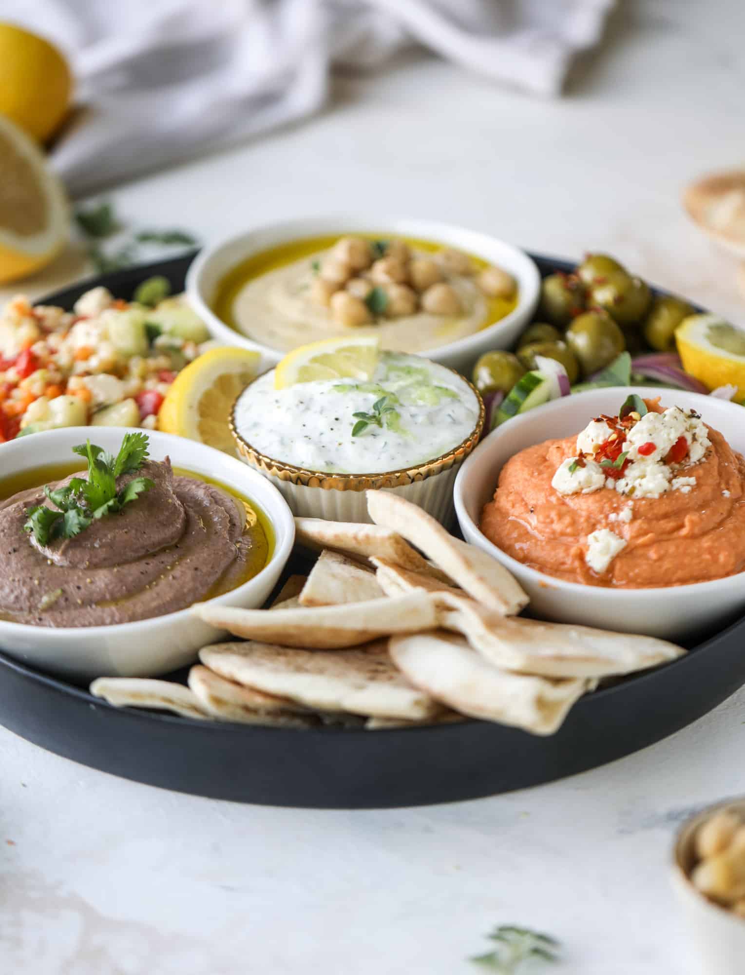 Here you can find out how to make the perfect hummus platter! This trio includes caramelized onion hummus, smoky black bean hummus and roasted red pepper white bean hummus, along with a couscous salad and quick tzatziki! I howsweeteats.com #hummus #platter #appetizer #snack #chickpeas #healthy #blackbeans #yogurt #tzatziki