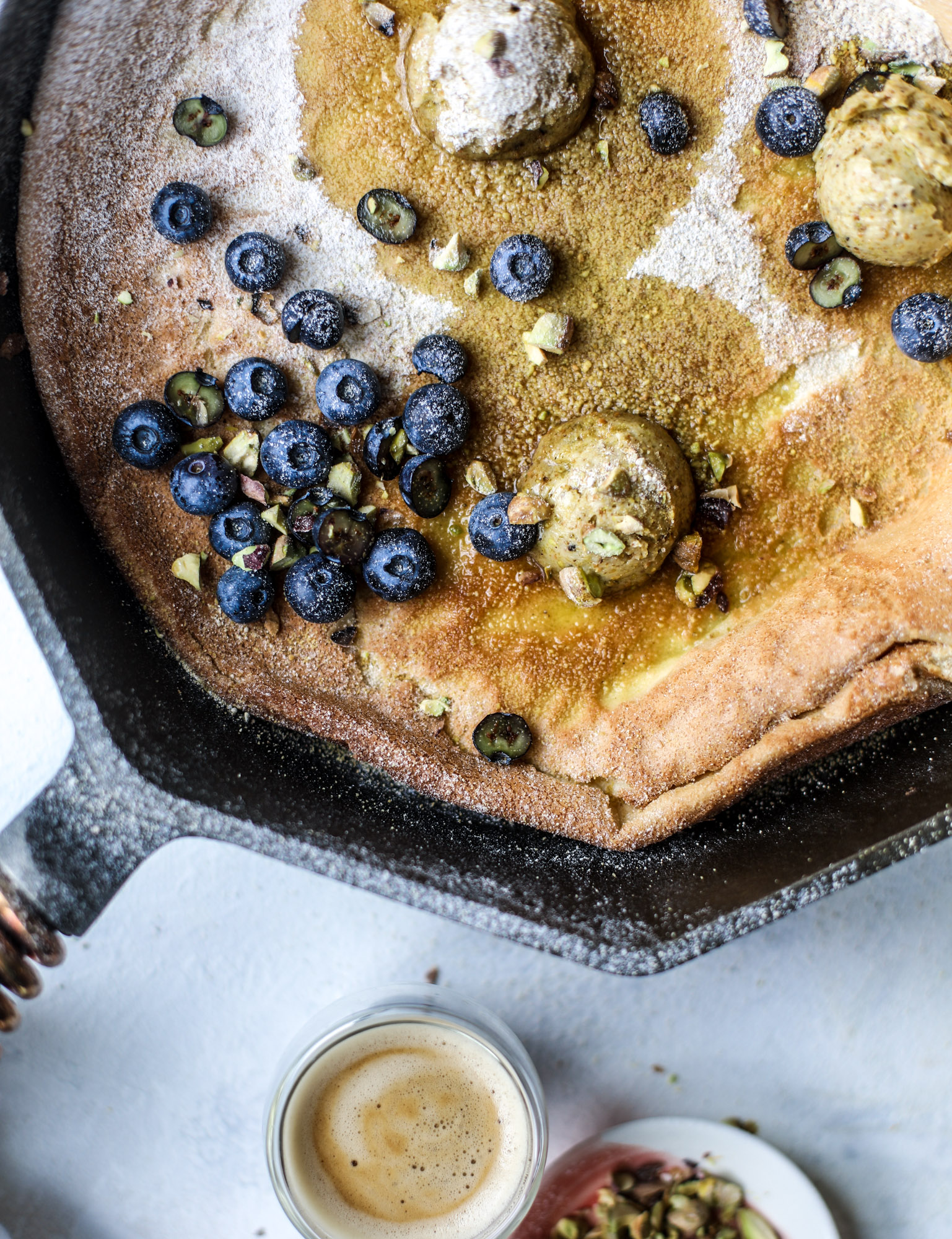 This incredible dutch baby recipe is fluffy and light and perfect for breakfast! It's sprinkled with pistachio sugar and served with pistachio butter and fresh blueberries. It's super easy, simple and always a hit! I howsweeteats.com #dutch #baby #pistachio #blueberry #breakfast