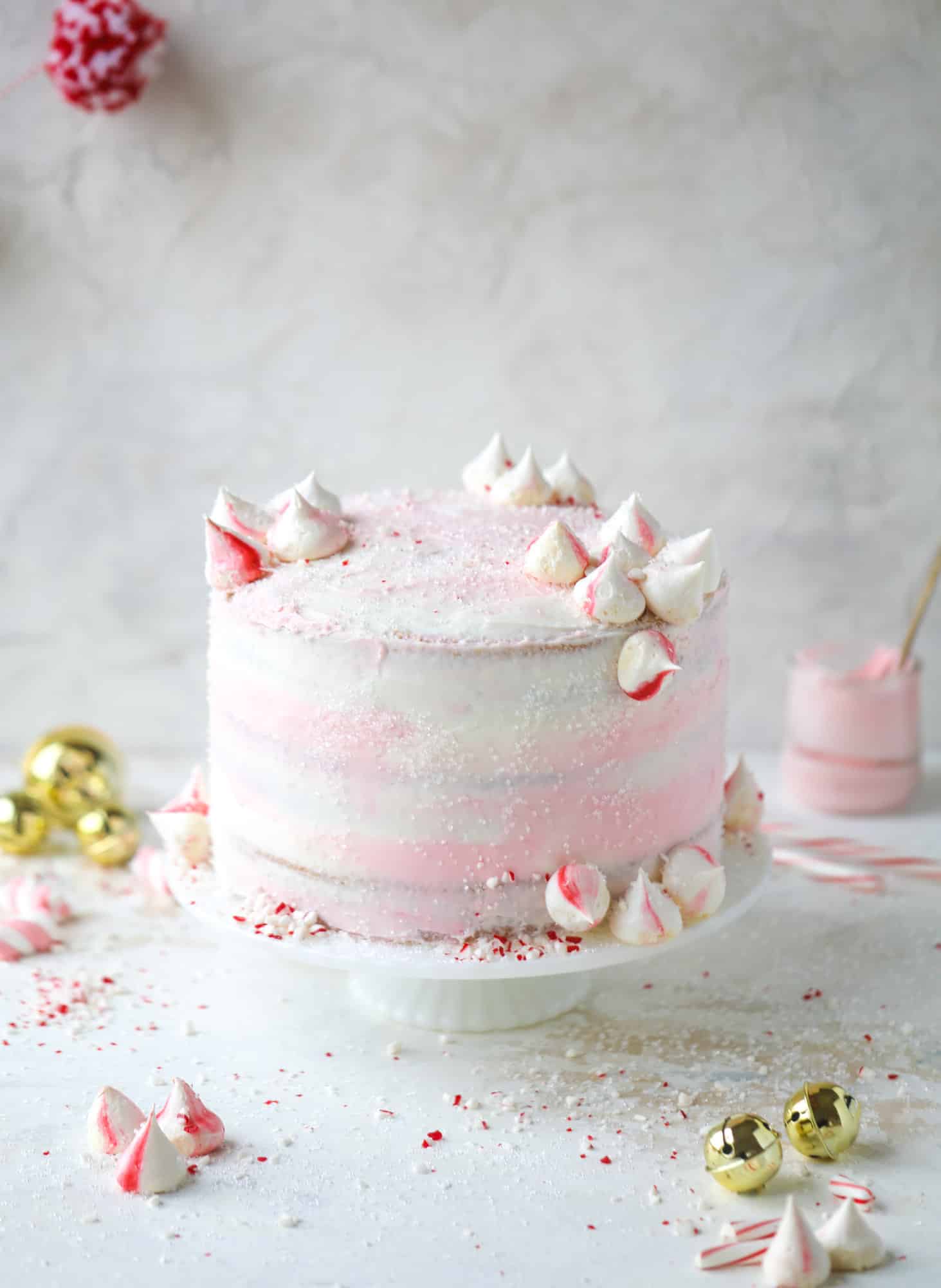 This pink peppermint cake is festive and delicious for the holidays! Layers of vanilla cake frosting with peppermint cream cheese frosting, covered in sparkly sugar and peppermint meringues. Couldn't be cuter! I #pinkpeppermint #cake
