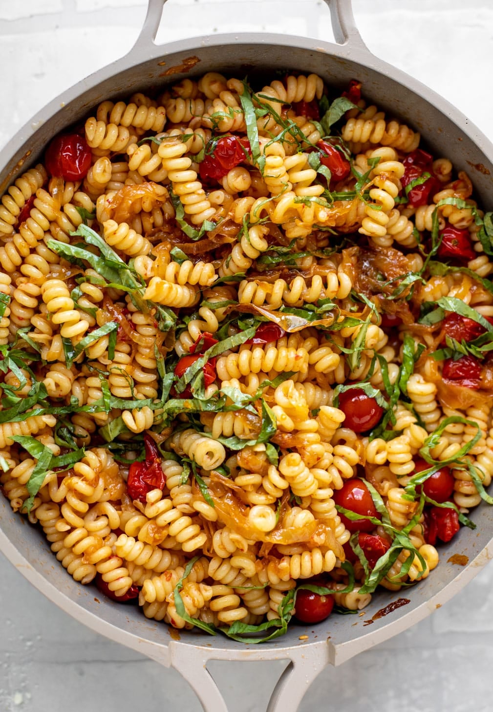 caramelized onion tomato pasta with basil in a skillet