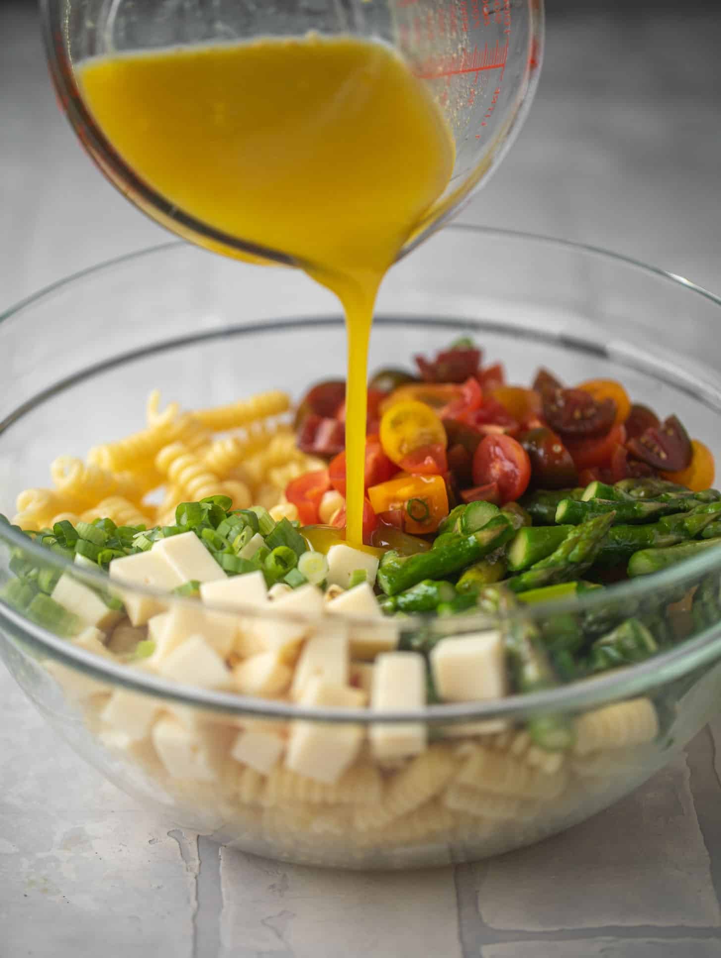pouring honey mustard dressing on asparagus pasta salad