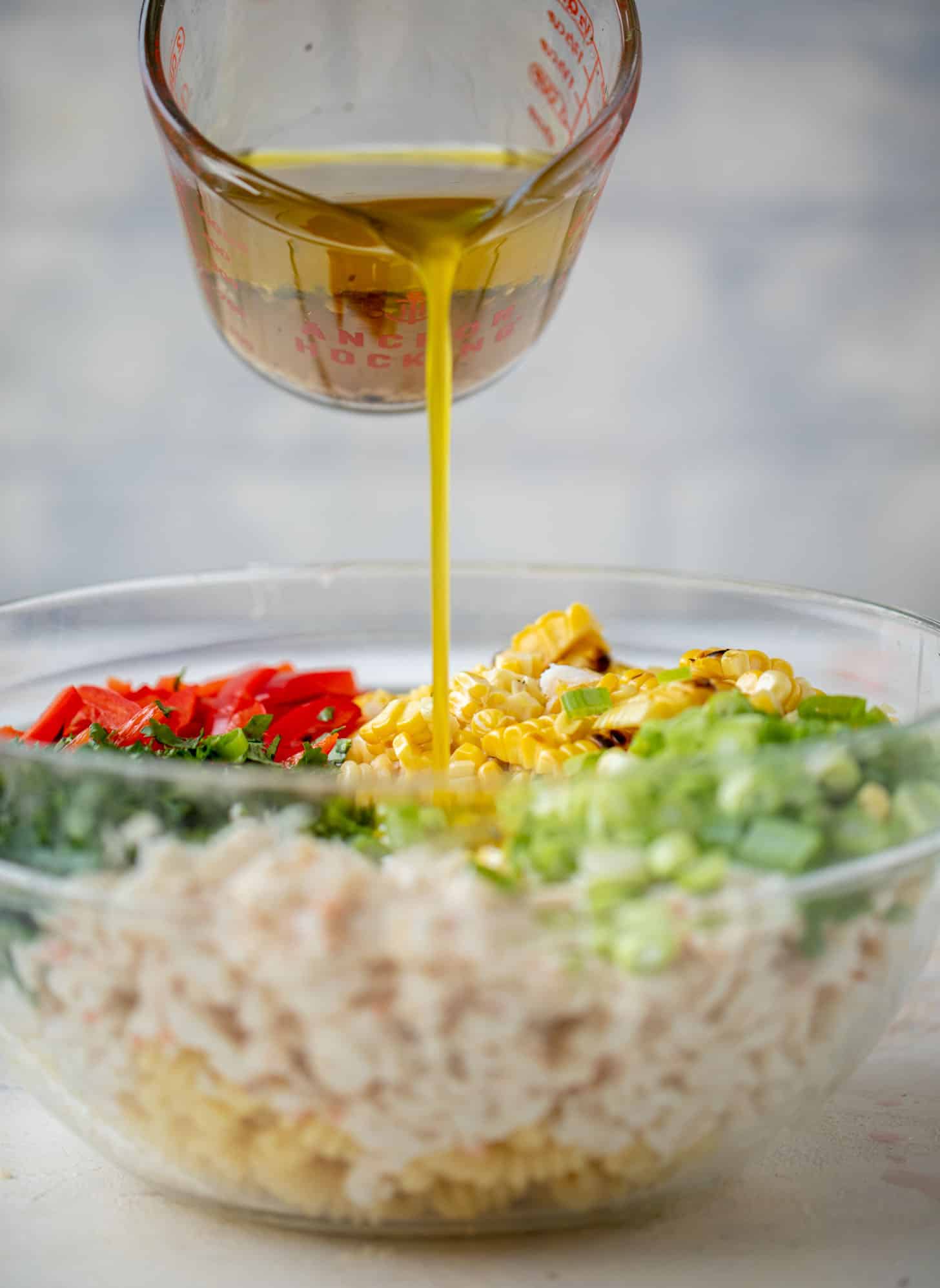 pouring dressing on grilled corn and crab pasta salad