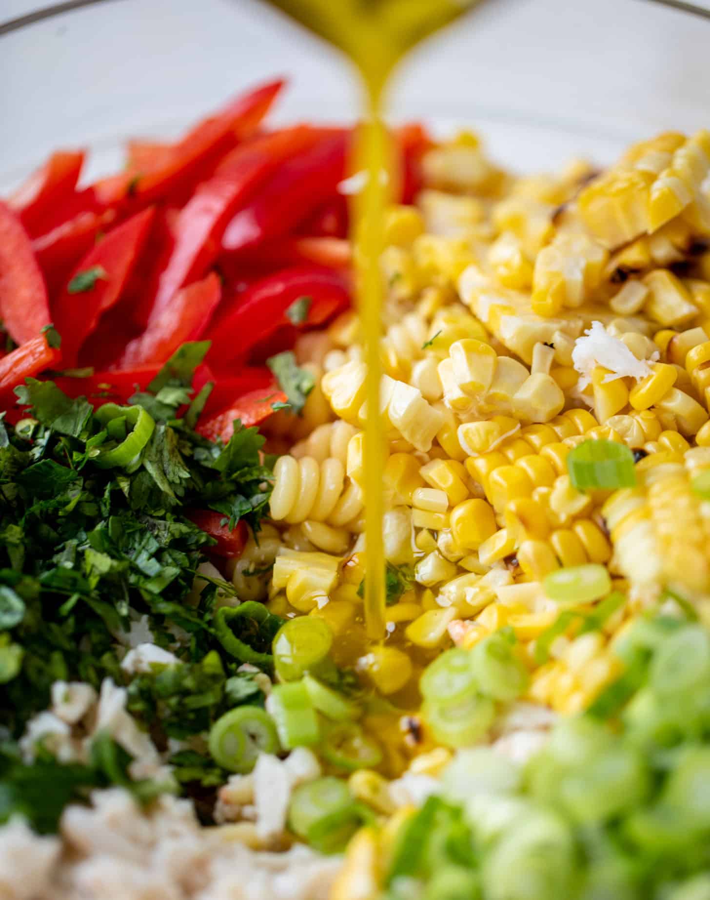 pouring dressing on grilled corn and crab pasta salad